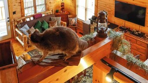 L’intérieur d’un chalet rustique, avec des murs en bois, un ventilateur de plafond, une cheminée, un téléviseur et une grande fenêtre.