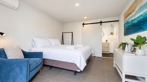 A modern bedroom with a bed, a blue sofa, a bedside table with a lamp, and a painting on the wall.