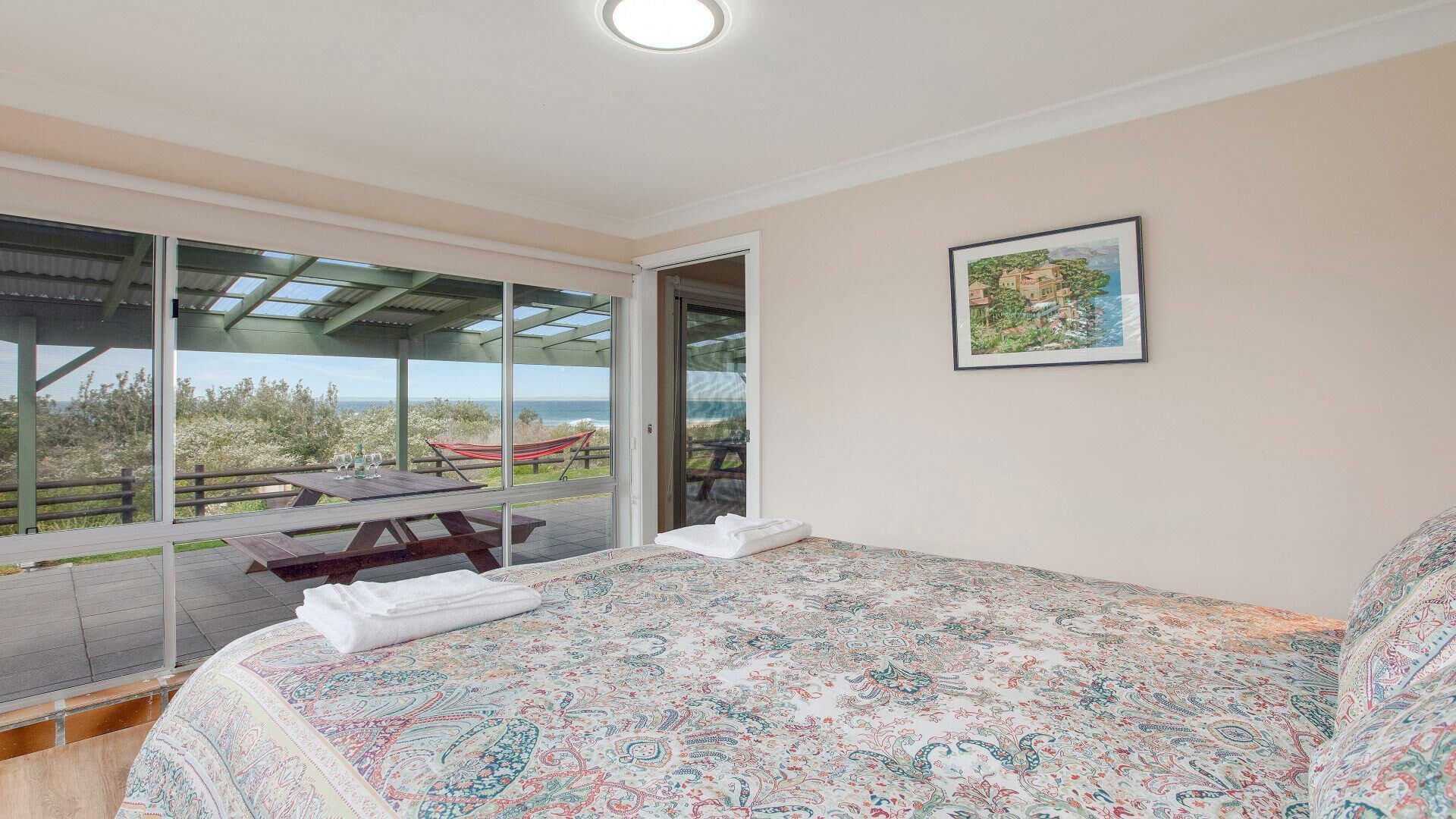 A bedroom with a large bed, a view of the sea, and a patio with a table and chairs.
