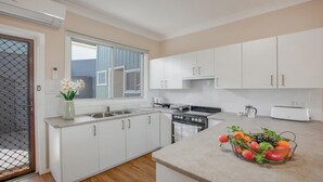 Een moderne keuken met witte kasten, een fornuis, een spoelbak en een broodrooster. Er is een raam met zonwering en een vaas met bloemen op het aanrecht.