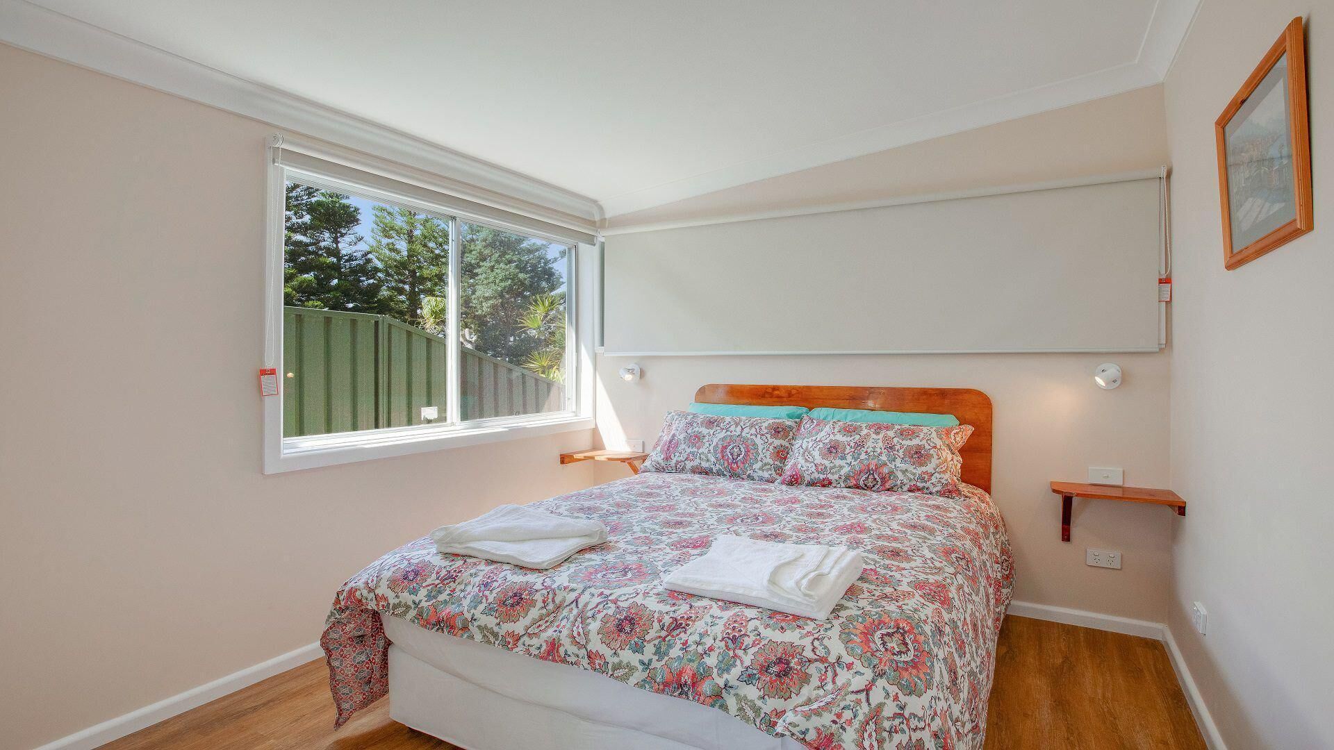 A bedroom with a bed, a window, and a wall-mounted shelf.