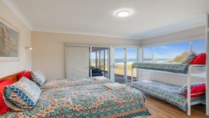 Een kamer met een bed, een stapelbed en een schuifdeur naar een balkon met uitzicht op het strand.