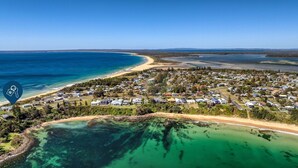 Luchtbeeld van een kustgebied met huizen, een strand en helderblauw water.