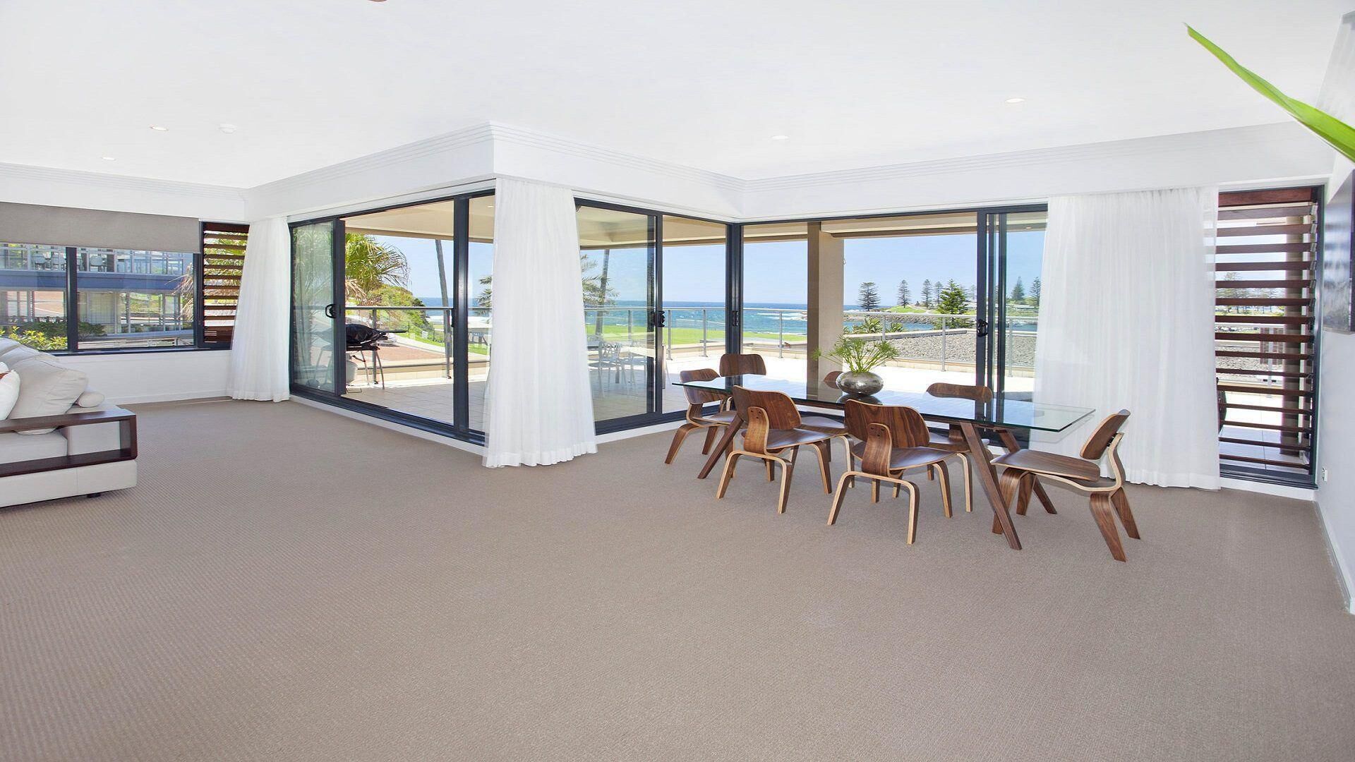 A spacious living room with a large glass door leading to a balcony with a view of the ocean.