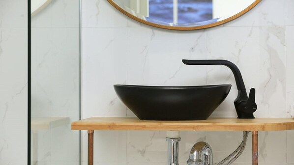 A black vessel sink with a curved faucet on a wooden countertop in a bathroom with white marble tiles.