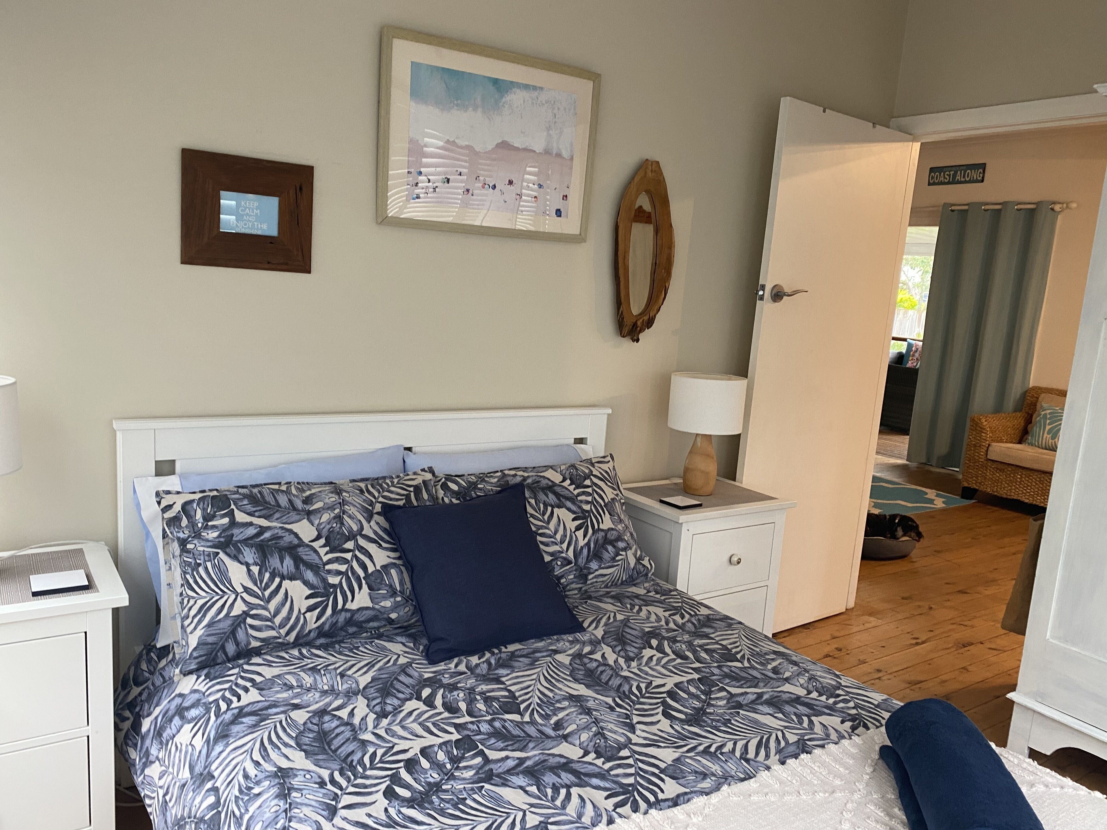A bedroom with a bed, nightstands, a lamp, a framed picture, and a door leading to another room.