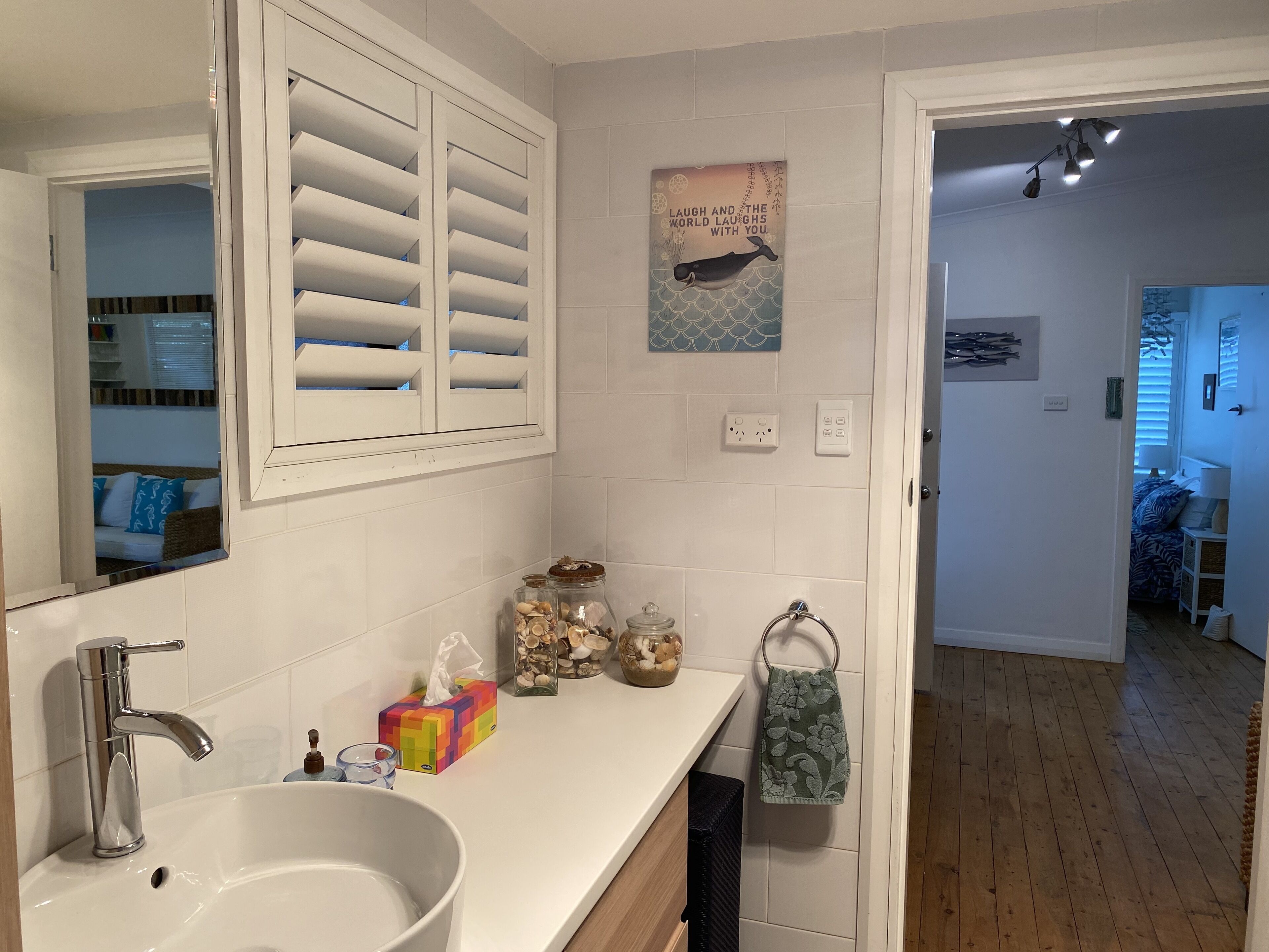 A bathroom with a white sink, a mirror, a towel rack, and a decorative wall piece.