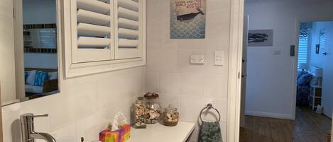 A bathroom with a white sink, a mirror, a towel rack, and a decorative wall piece.
