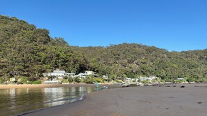 A beach with a clear view of a coastal house complex, a sandy beach, and a forested hillside. - The Beach House - close to everything! (Patonga)