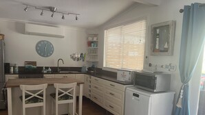 A kitchen with a wooden table, two chairs, a refrigerator, a microwave, and a clock on the wall. - The Beach House - close to everything! (Patonga)