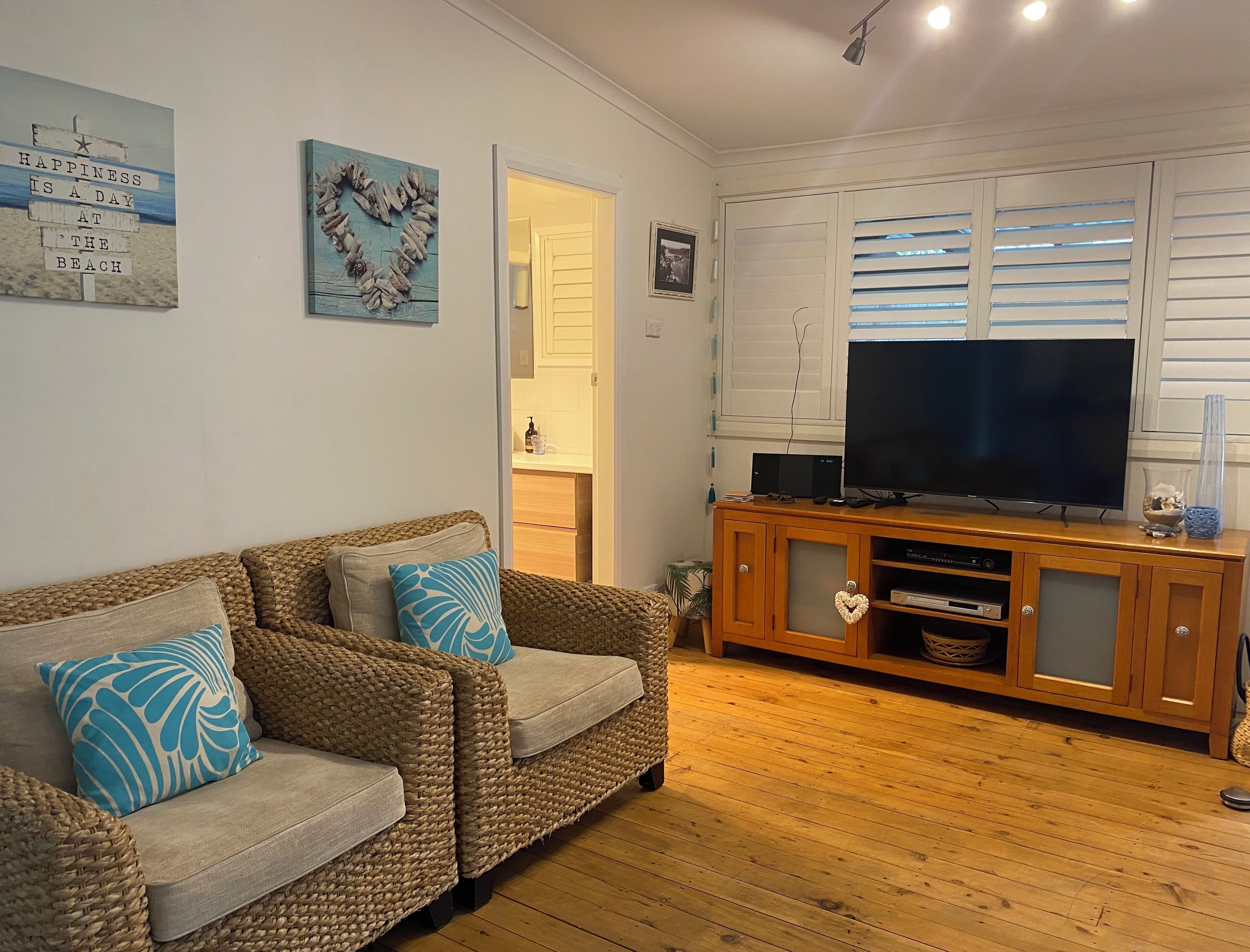 A cozy living room with a woven sofa, wooden entertainment unit, and a large TV.