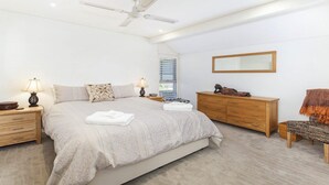 A modern bedroom with a large bed, wooden dresser, and a ceiling fan.
