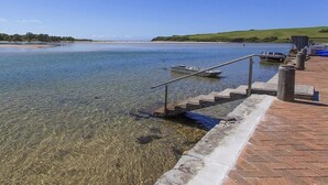 A clear waterfront with a boat dock, a stone staircase leading into the water, and a grassy hillside in the background.