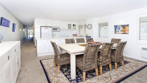 A modern kitchen with white cabinetry, a dining area with a light-colored table and woven chairs, and a patterned rug.