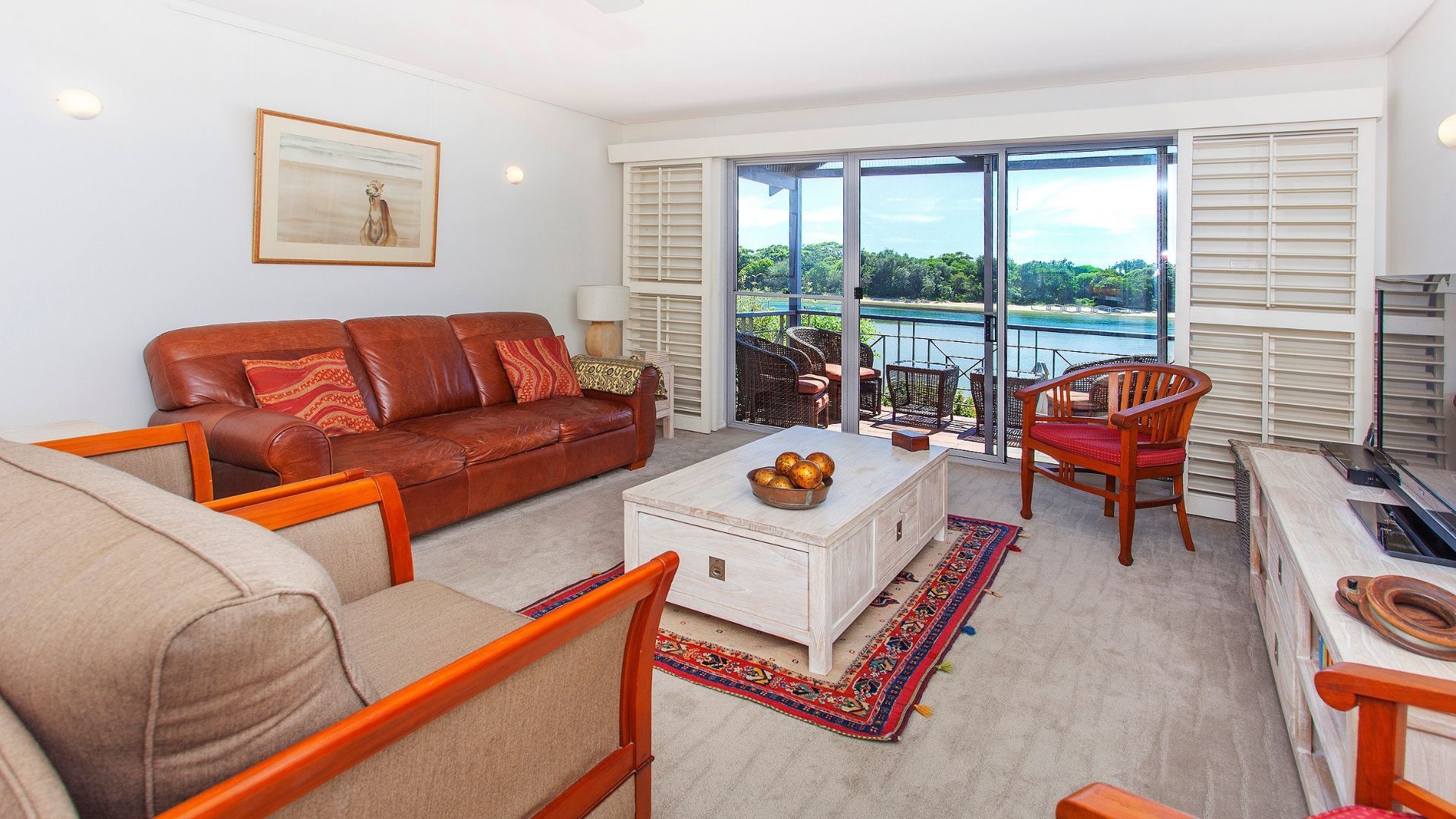 A living room with a sofa, chairs, a coffee table, and a view of a body of water through large sliding doors.