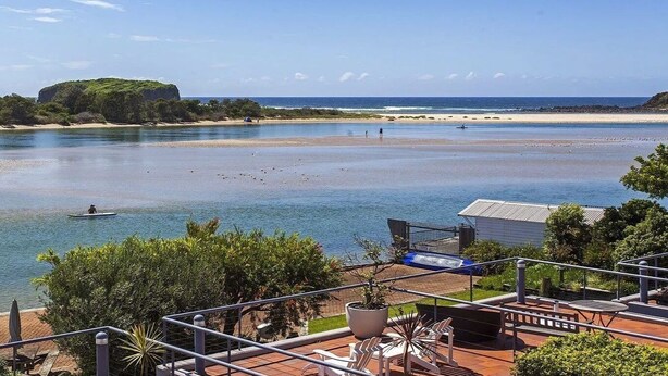 A coastal view with a beach, a boat, and a building with outdoor seating.