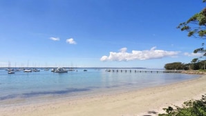 A beach with clear water, a sandy shore, and a pier extending into the sea.