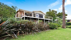 A modern two-story house with a balcony, surrounded by lush greenery and a well-maintained lawn.