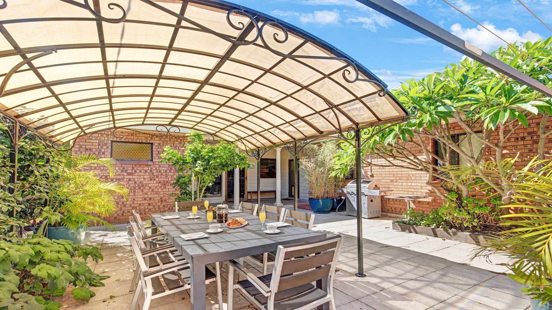 A covered patio with a brick wall, outdoor seating, and various plants.