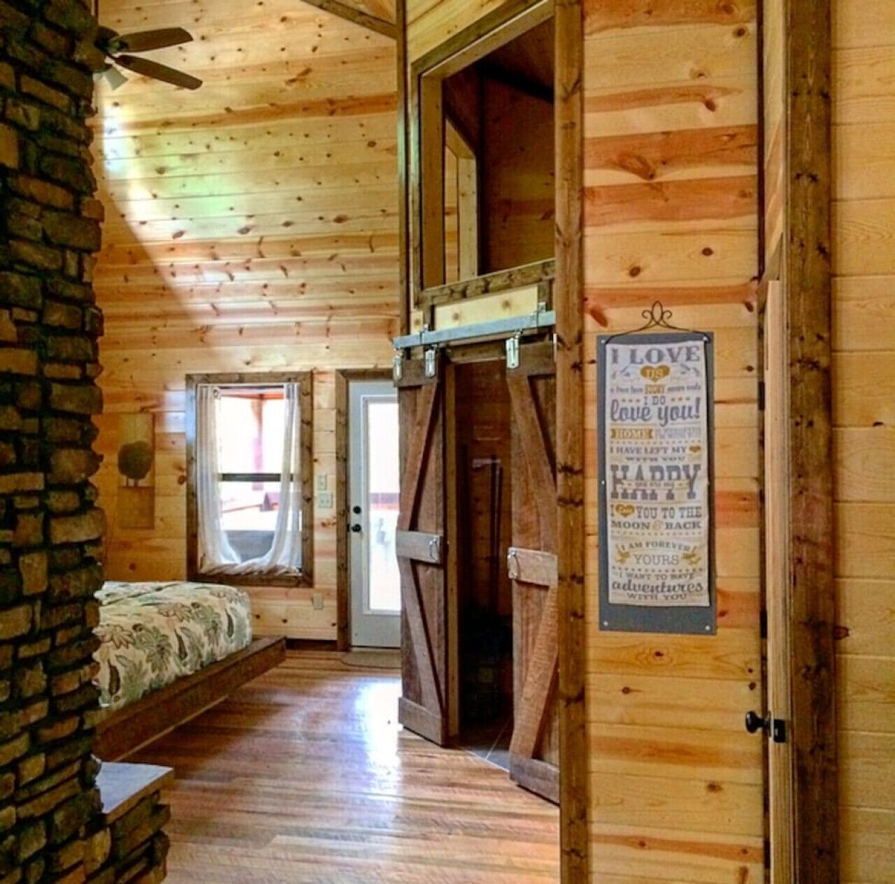 Une cabane chaleureuse aux murs en bois et dotée d’un lit en mezzanine. Une pancarte accrochée au mur porte l’inscription : « J’aime ma maison. »
