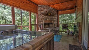 Una cabaña de madera con chimenea de piedra, un jacuzzi y una terraza con vistas a un bosque.