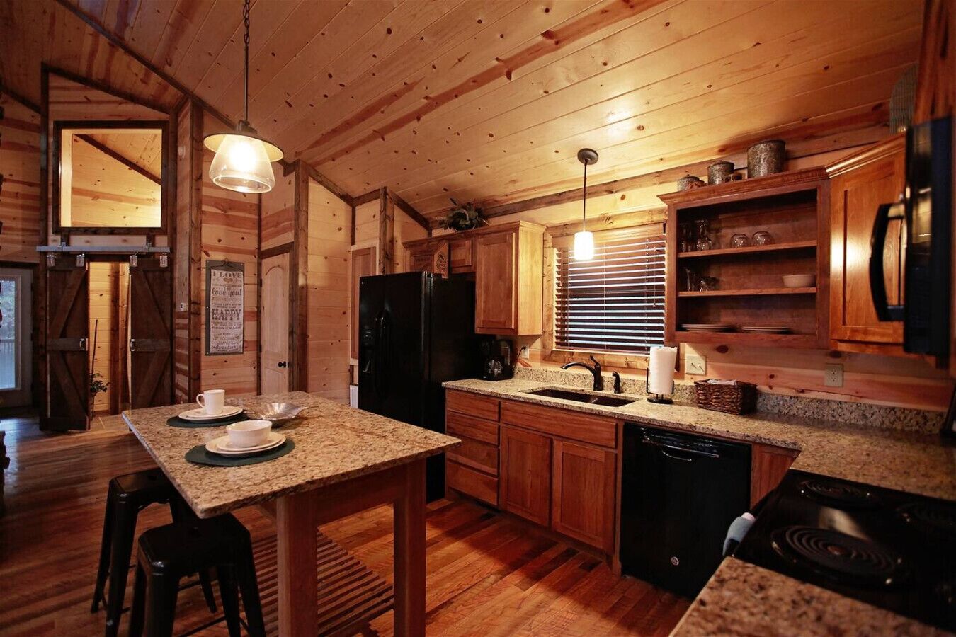 A cozy cabin-style kitchen with wooden cabinets, granite countertops, a black refrigerator, and a built-in dishwasher.