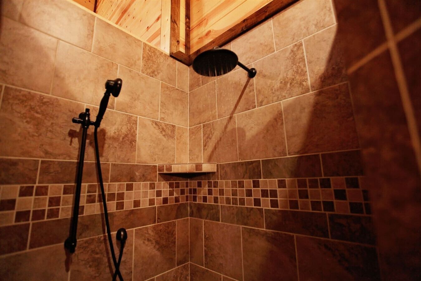 Ein Duschbereich mit Holzboden, gefliesten Wänden und einer Handbrause.