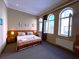 Hotelkamer met een groot bed, twee nachtkastjes, een radiator en drie ramen.