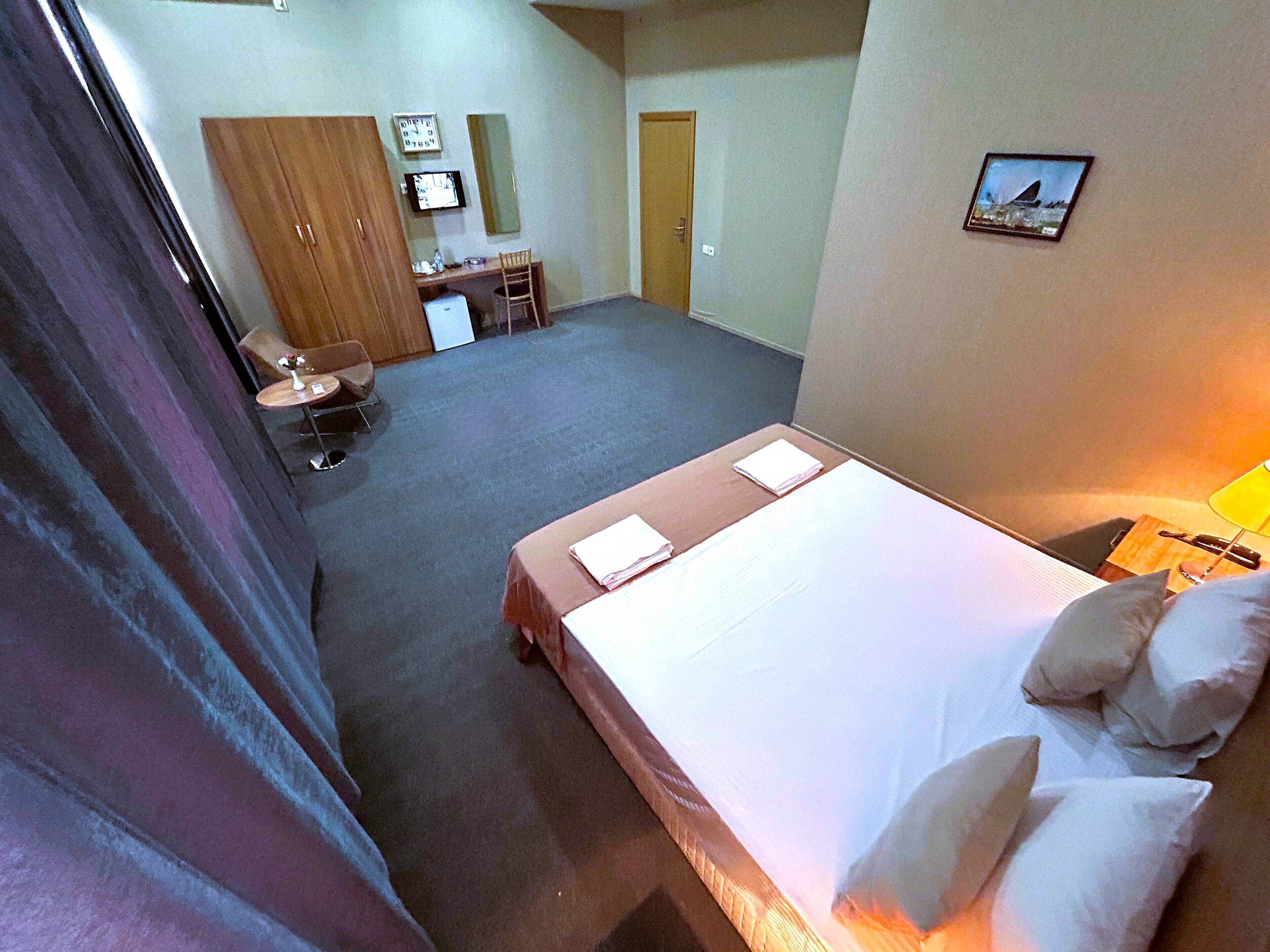 Quarto de hotel com cama, escrivaninha, cadeira e mesa pequena com abajur.