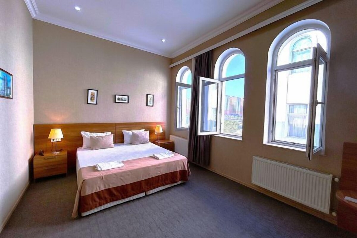 A hotel room with a large bed, two bedside tables, a window with curtains, and a radiator.