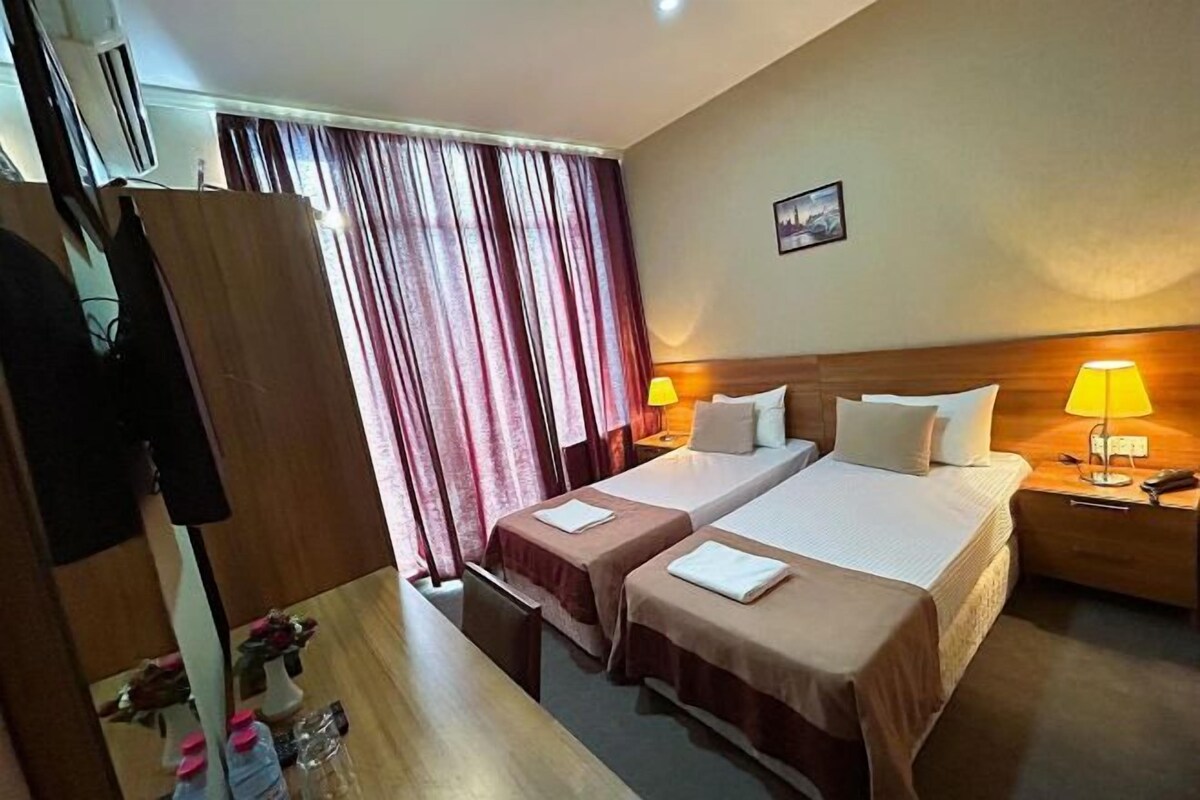 A hotel room with two beds, a wooden wardrobe, a mirror, and a window with curtains.