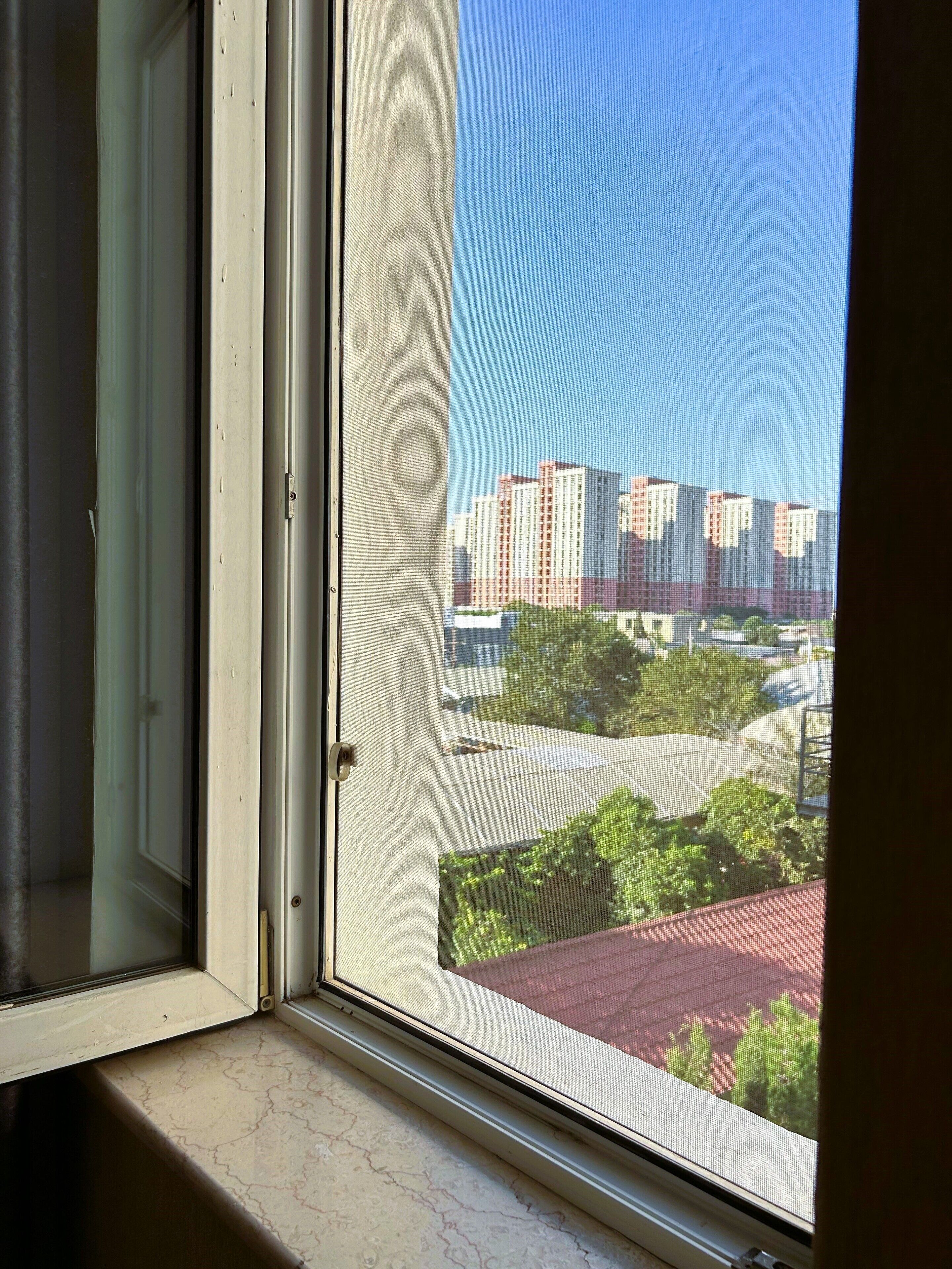 Une fenêtre donnant sur un paysage urbain, avec des gratte-ciel et des espaces verts.