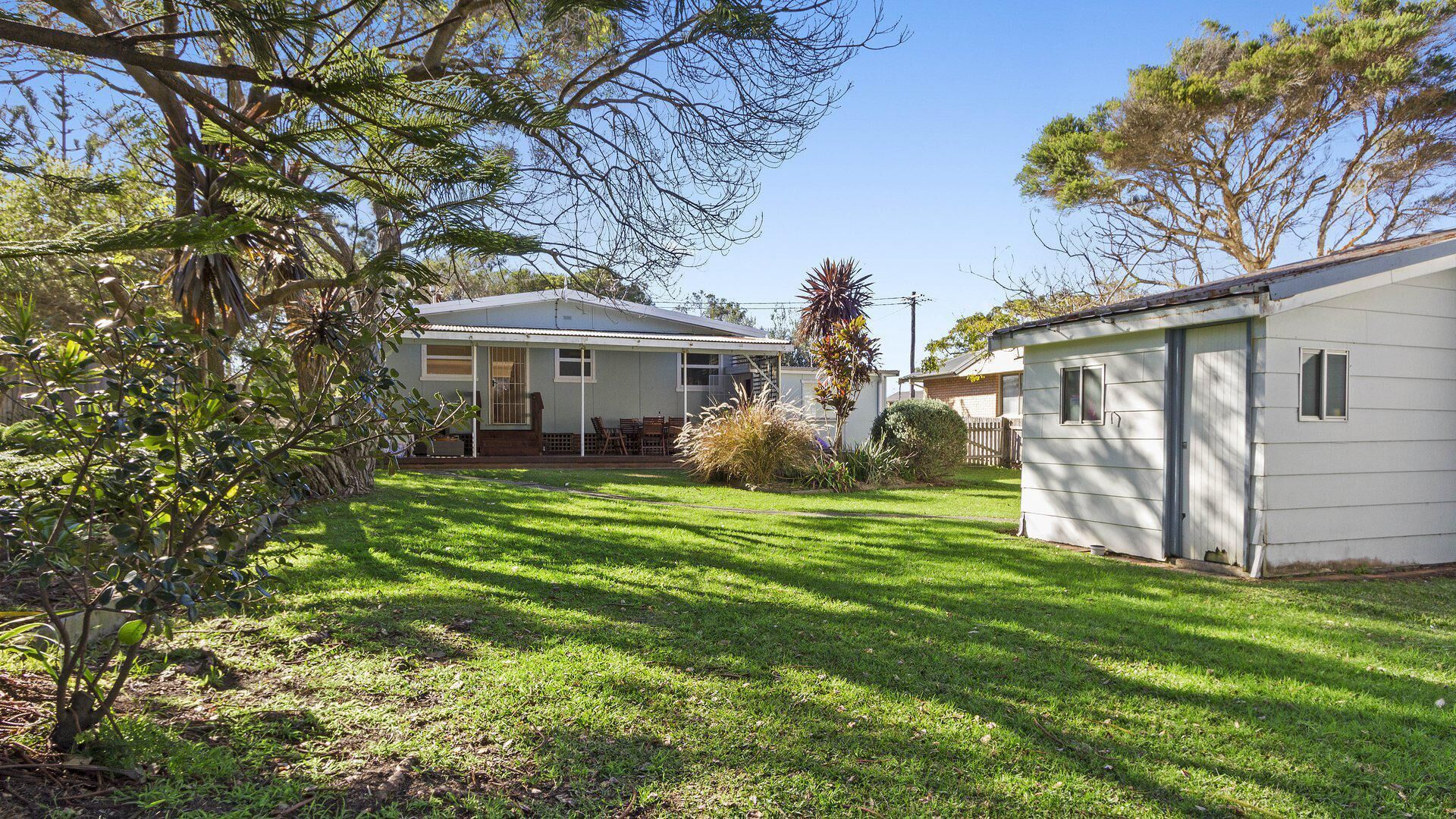 Une maison à deux étages avec un patio couvert et un petit abri de jardin.