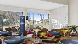 A dining table set with glasses of whisky, a bottle of whisky, and various fruits and cheeses. - Between 2 Beaches – pet friendly cottage (Culburra Beach)