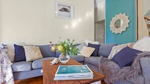 A living room with a grey sofa, a wooden coffee table with books, a vase with flowers, and a framed picture on the wall. - Between 2 Beaches – pet friendly cottage (Culburra Beach)