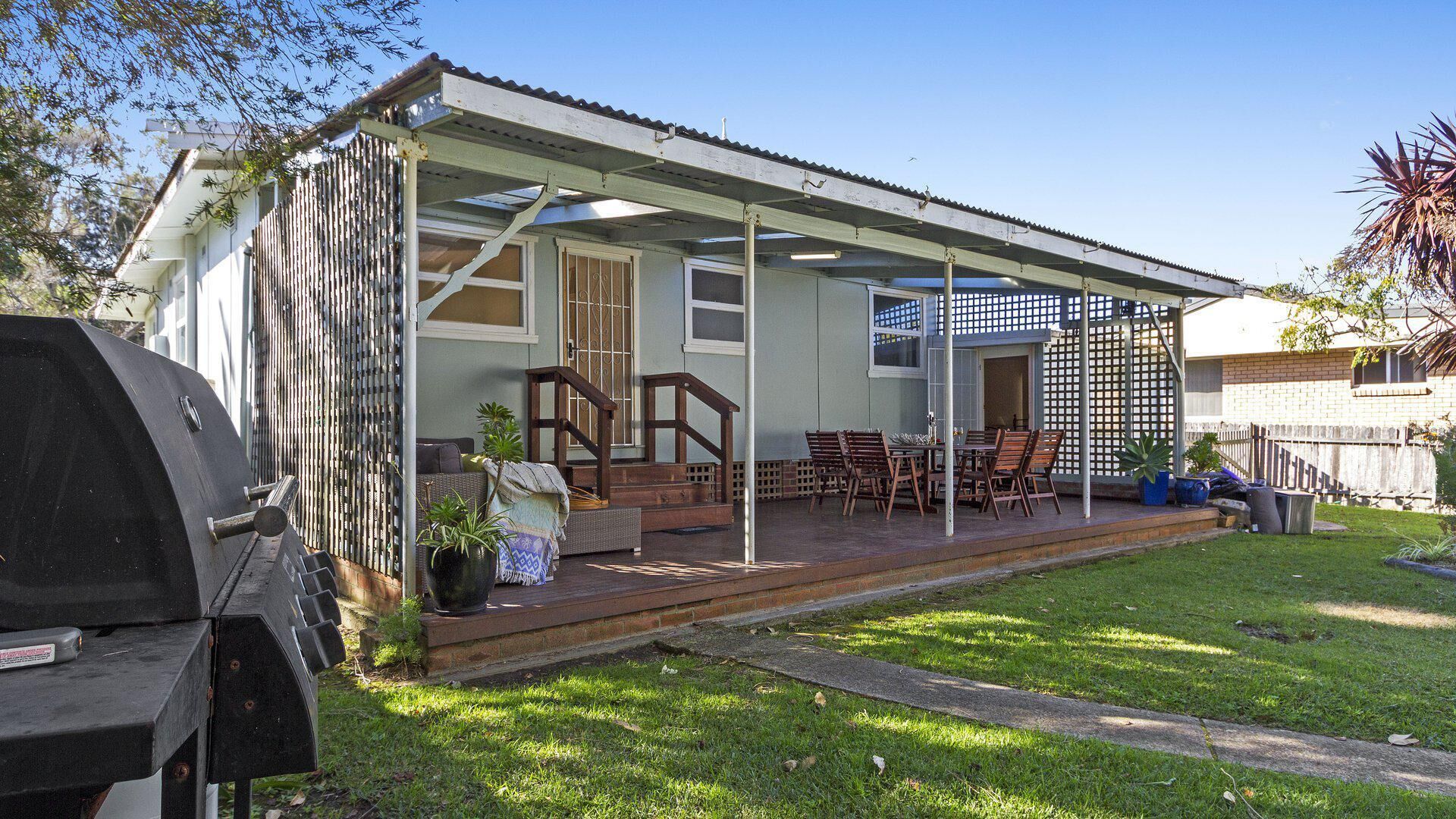 A covered outdoor patio with a dining area, a barbecue grill, and a fenced garden.