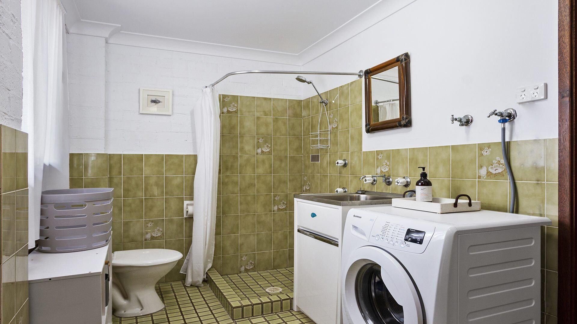 Ein kleines Badezimmer mit Toilette, Waschmaschine und Duschbereich.