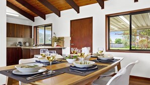 A dining area with a wooden table set for a meal, surrounded by white chairs. - Sea Bird – unplug unwind and enjoy (Culburra Beach)