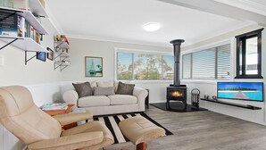 Ein Wohnzimmer mit einem beigen Sofa, einem schwarz-weißen Teppich, einem Kamin, einem Fernseher und einem Bücherregal.