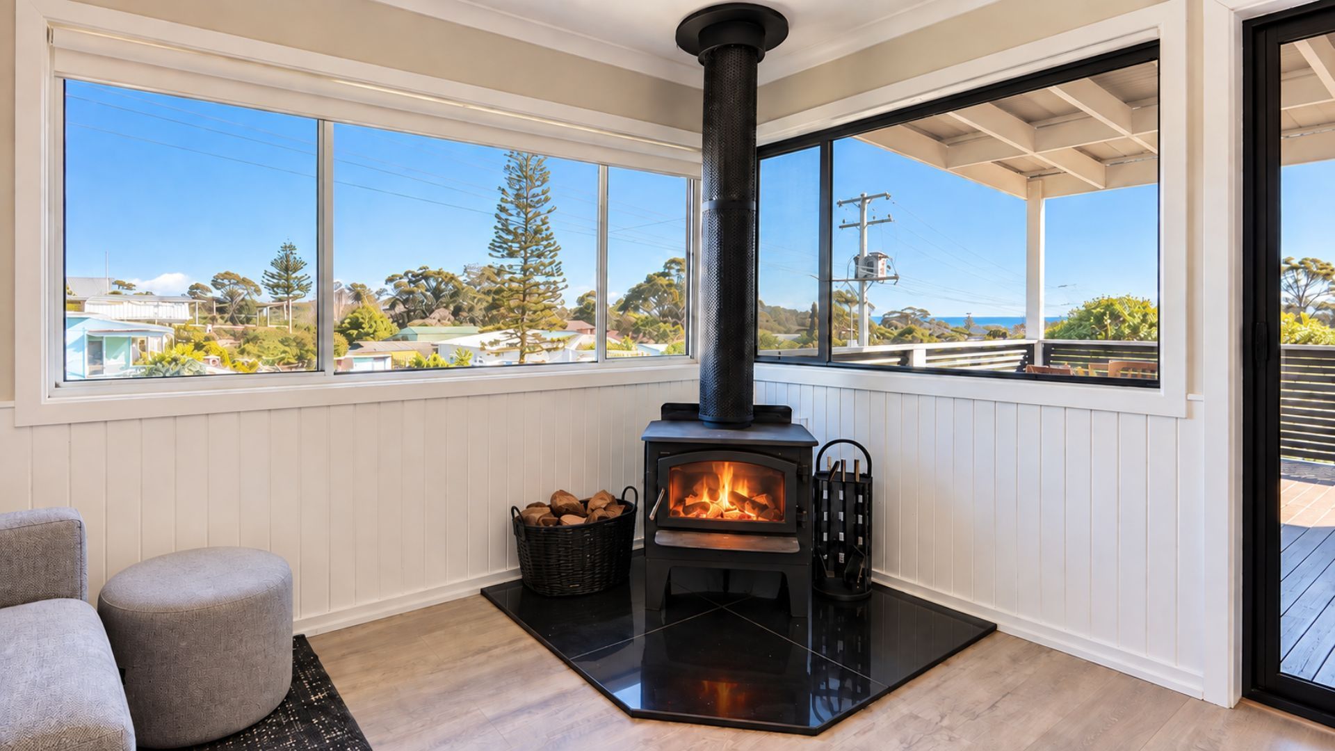 A room with a wood-burning stove, a view through large windows, and a seating area with a rug.