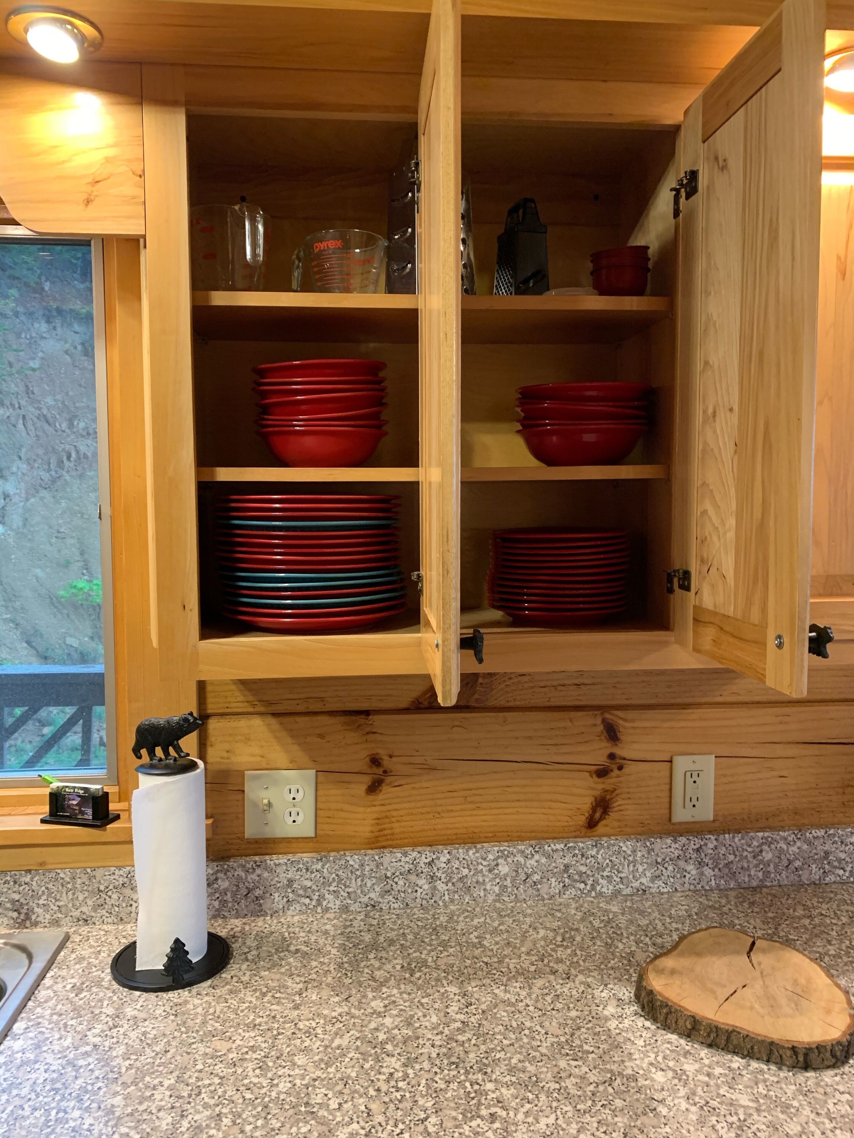 Un meuble de cuisine en bois, doté de plusieurs étagères où sont rangées des assiettes rouges et bleues, un verre doseur et un objet noir.