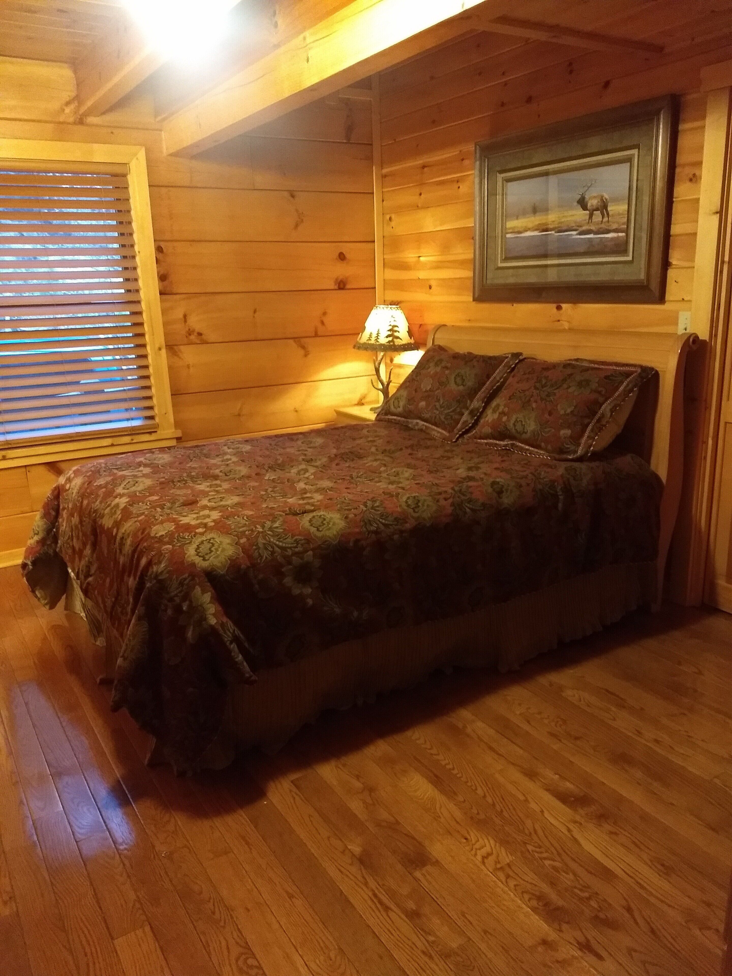 A wooden cabin bedroom with a bed, a lamp, and a framed picture on the wall.