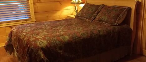A wooden cabin bedroom with a bed, a lamp, and a framed picture on the wall.