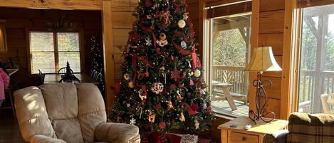 A cozy cabin interior with a decorated Christmas tree, plush seating, and a wooden floor.