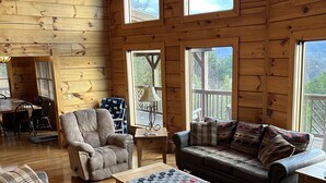 A cozy cabin interior with wooden walls, a dining area, a sofa, a coffee table, and a view of the outdoors. - Breathtaking mountain and sunset views...huge cabin with cozy atmosphere (Pigeon Forge)
