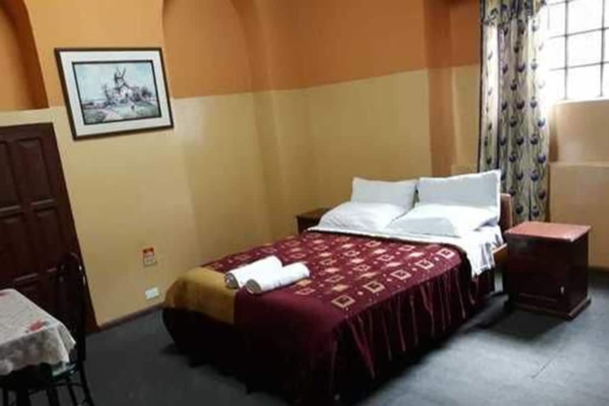A hotel room with a bed, a chair, a table, and a painting on the wall.