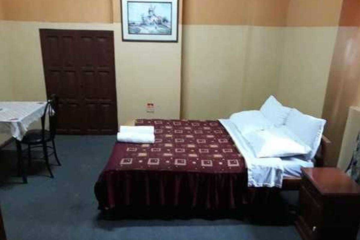 A small, simple room with a bed, a chair, a table, and a wardrobe.