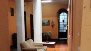Um corredor amplo com um sofá bege, piso ladrilhado e uma janela grande com vista.