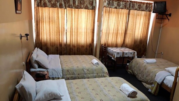 Quarto de hotel com duas camas, uma mesinha e uma televisão.