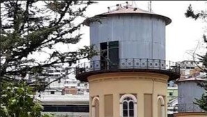 Um edifício com uma torre redonda, janelas em arco e um pátio pavimentado.